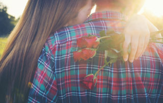 A young women holding roses embraces a man